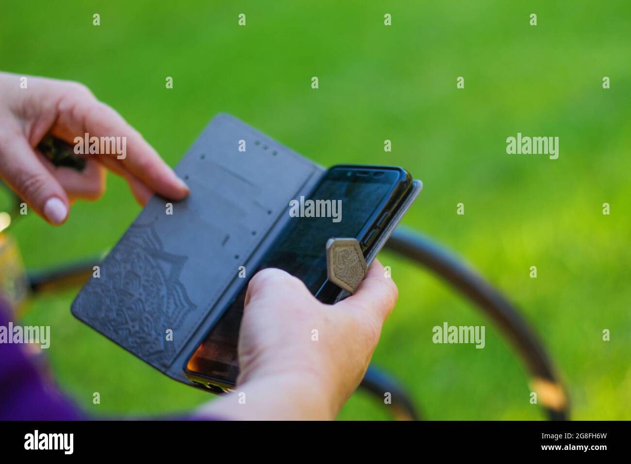 Unschärfe-Effekte bei Nahaufnahme von weiblichen Händen, die sich außerhalb des Telefons berühren. Frau in lila Bluse mit Smartphone, während sie auf einer Bank im Park sitzt. Co Stockfoto