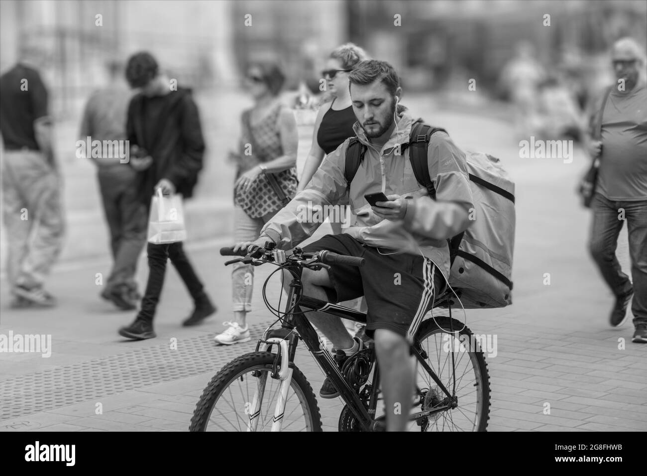 Pizza-Typ auf einem Fahrrad, trägt einen Rucksack und benutzt ein Handy, während er eine Straße in York, North Yorkshire, England, fährt. Stockfoto