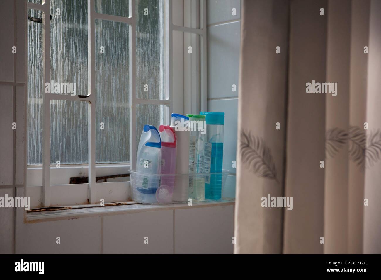 East Sussex, Großbritannien, 17. Juli 2021: Plastikflaschen mit Duschgel auf einer Fensterbank neben einem Duschvorhang. Das Milchglasfenster leuchtet sanft auf Stockfoto