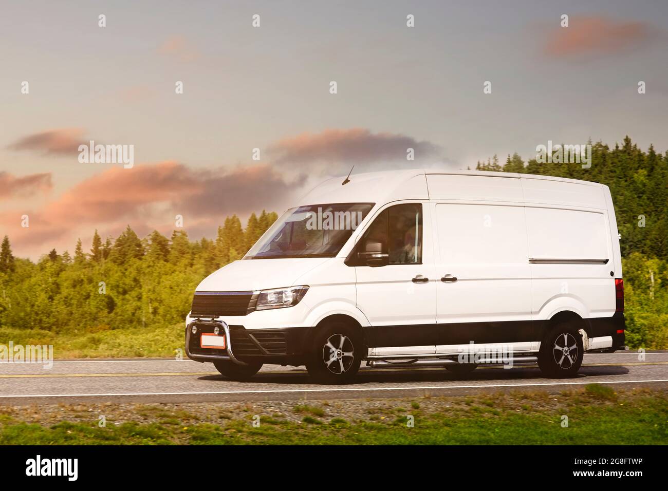 Weißer Lieferwagen transportiert Waren im goldenen Licht des Sonnenuntergangs entlang der Straße. Stockfoto