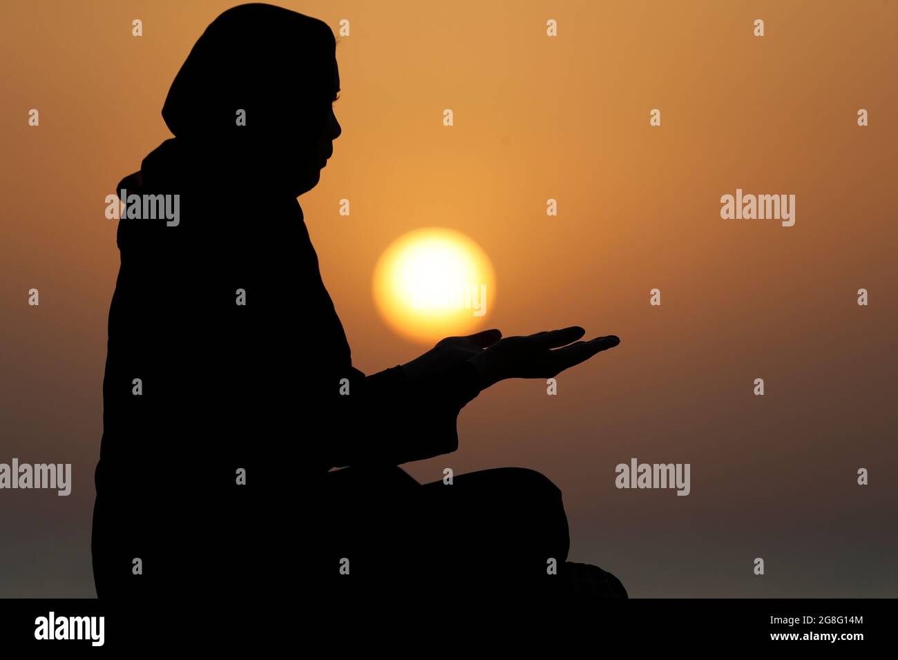 Silhouette einer muslimischen Frau in Abaya, die bei Sonnenuntergang mit ihren Händen betet, Vereinigte Arabische Emirate, Naher Osten Stockfoto