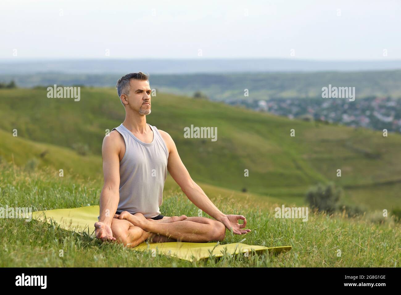 Yoga in der Natur. Ein bärtiger, nicht junger Mann praktiziert Yoga-Meditation, sitzt in einer Lotusposition auf dem Gras auf der Sommernatur. Stockfoto