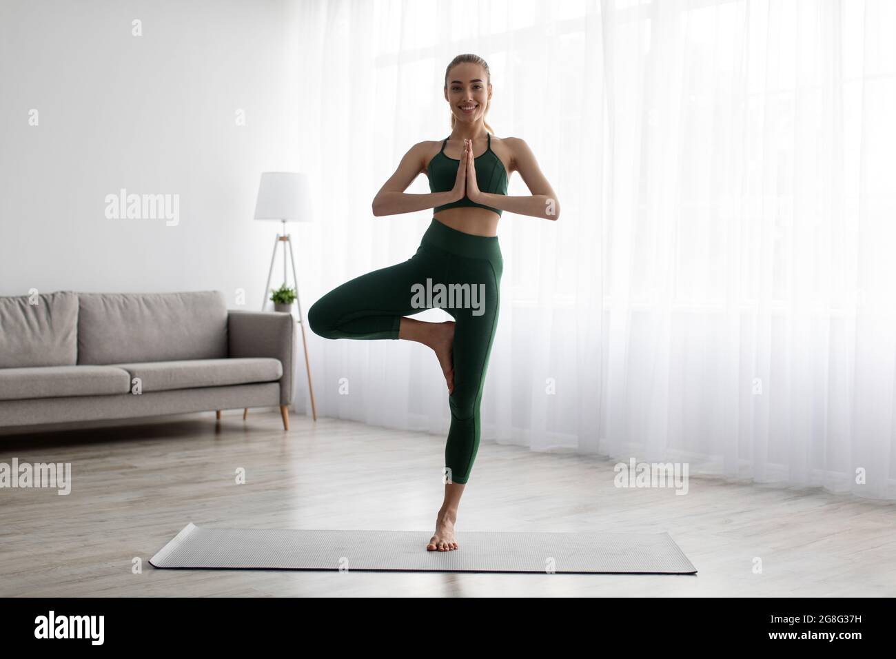 Ruhige junge Frau, die Yoga praktiziert, Übungen im Wohnzimmer, gesunder Lebensstil Stockfoto