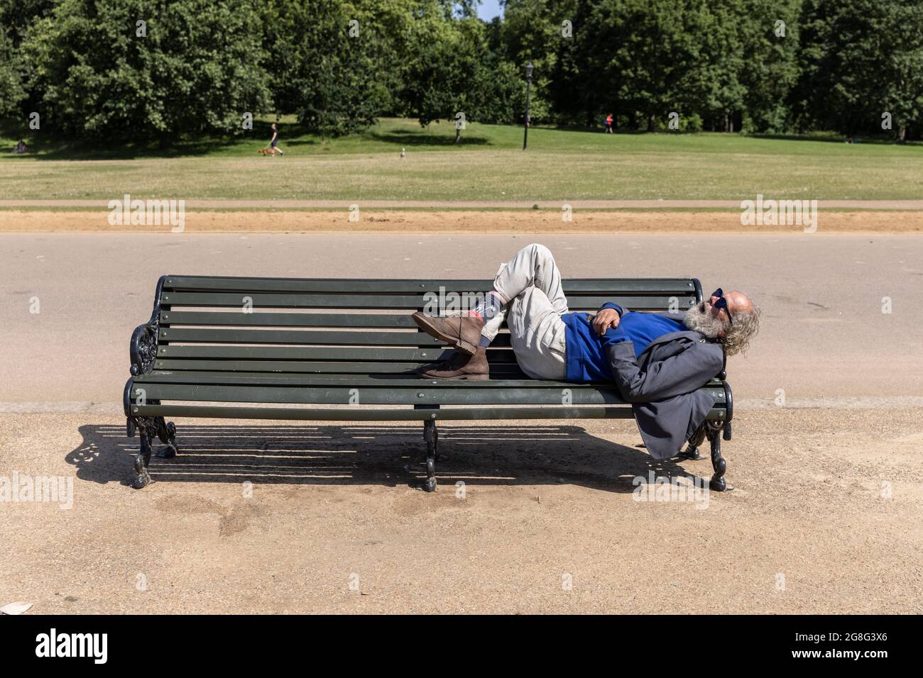 An einem heißen Sommertag im Hyde Park, Central London, England, entspannt sich ein Mann auf einer Parkbank am Rande des Serpentine Stockfoto