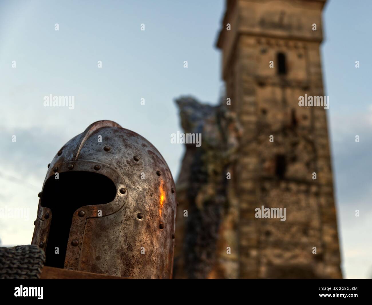 Nahaufnahme eines Helms, der auf einer Kettenpost mit einem romanischen Glockenturm im Hintergrund ruht Stockfoto