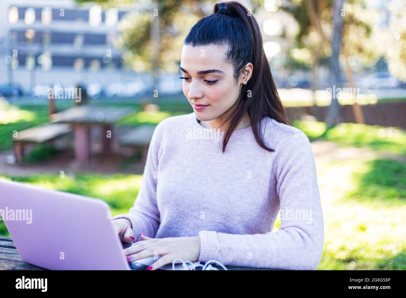 Junge schöne Frau, die im Freien sitzt, während sie mit dem Computer arbeitet Stockfoto