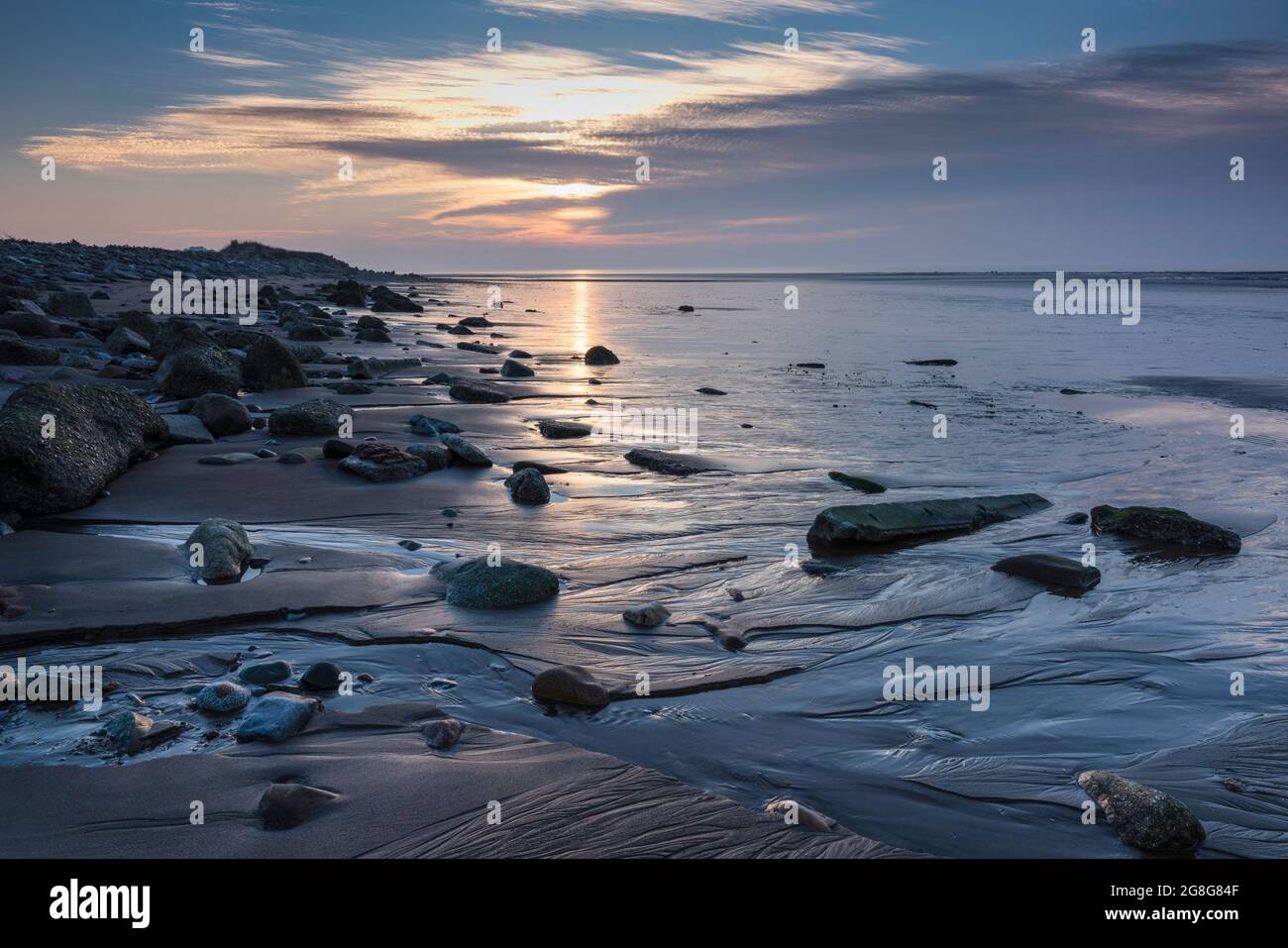 Sonnenuntergang über der Küste von Solway Firth, mit Reflexionen auf Sand und Felsen während einer nachlassenden Flut. In der Nähe von Allonby, nordwestlich von Cumbria, England Stockfoto
