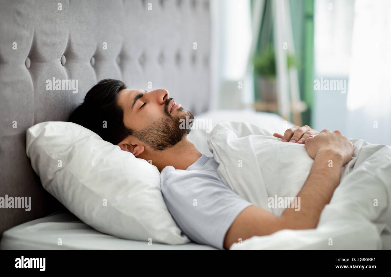 Tiefer Männerschlaf. Der junge araber schläft friedlich in seinem bequemen Bett zu Hause und liegt mit geschlossenen Augen auf dem Rücken Stockfoto