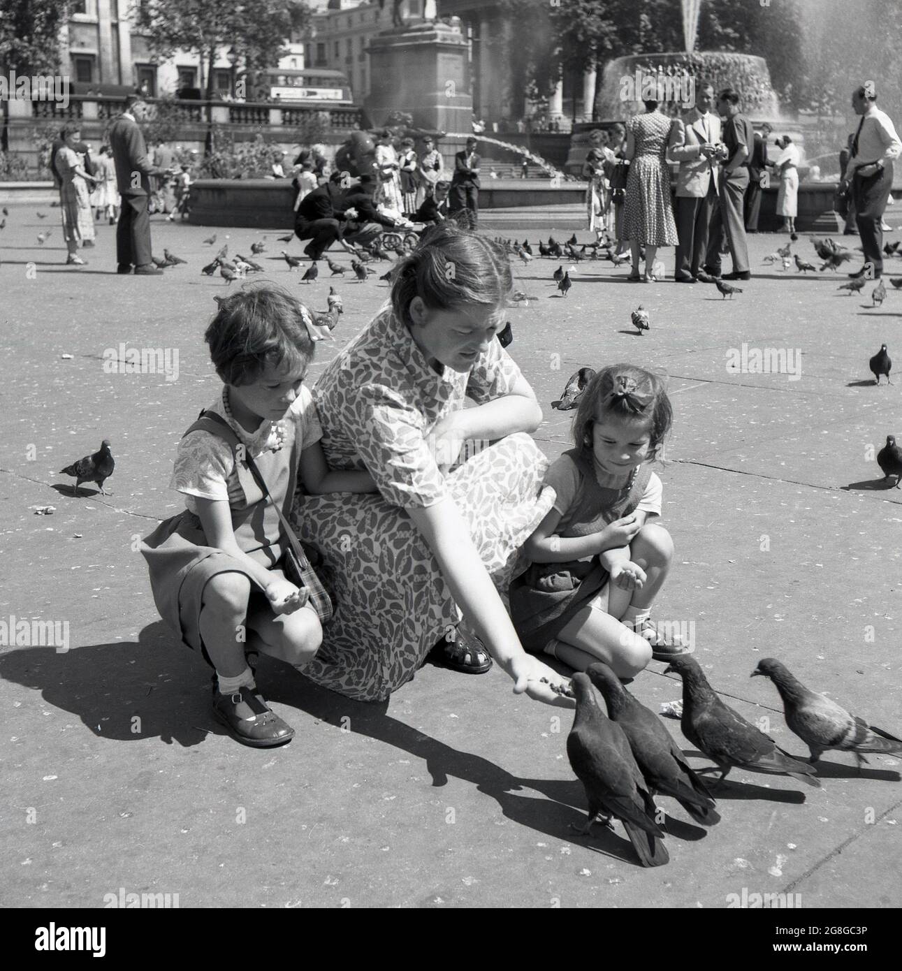 In den 1950er Jahren, mit ihren zwei jungen Töchtern neben ihr, fütterte eine Dame die Tauben am Trafalgar Square, London, England, Großbritannien. Eine traditionelle Aktivität seit mehr als hundert Jahren, wurden Schwärme von Tauben auf den Platz herabsteigen, um Nahrung von denen zu erhalten, die das berühmte Wahrzeichen von Central London besuchen. Stockfoto