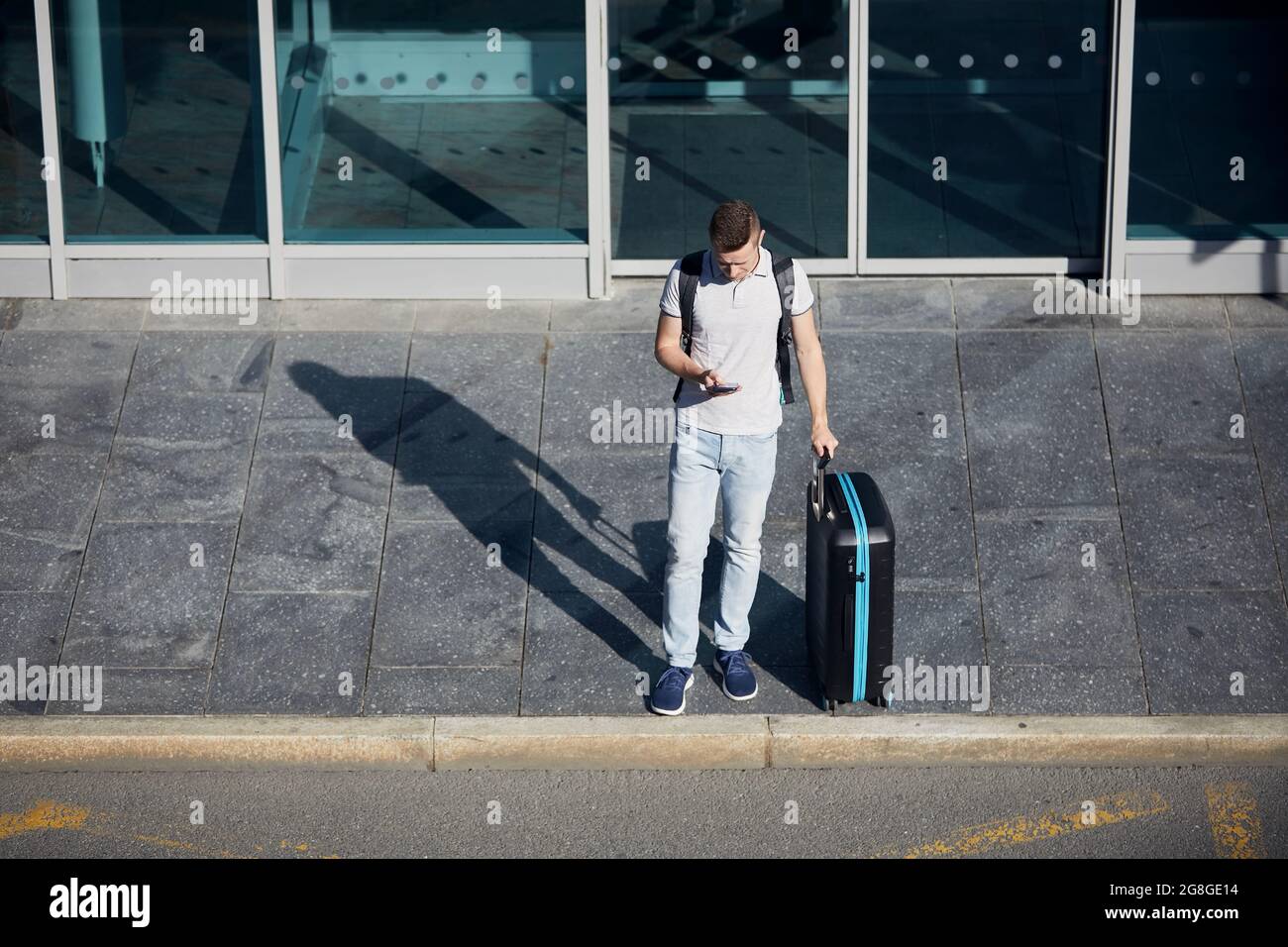 Mann, der die mobile App auf dem Smartphone verwendet. Passagier mit Suitcace wartet auf der Stadtstraße. Stockfoto