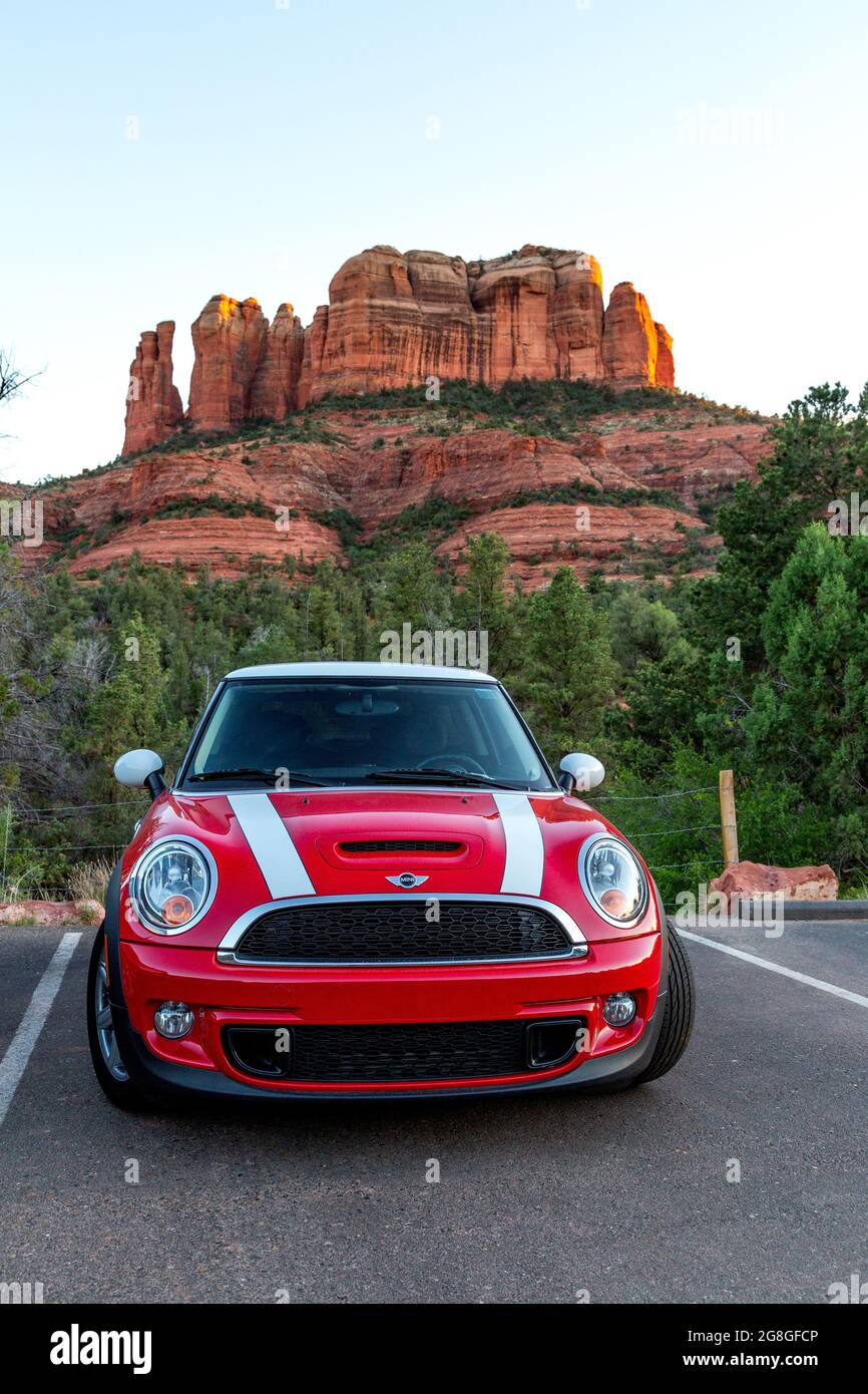 SEDONA, ARIZONA / US - 10. August 2019: Red Mini Cooper S mit weißen Rennstreifen, die bei Sonnenuntergang vor dem Cathedral Rock über roten Felsklippen geparkt sind. Stockfoto