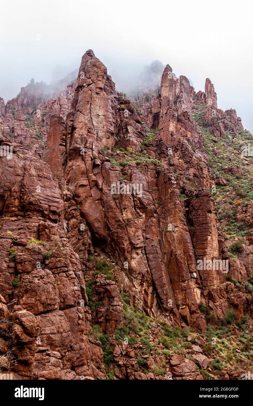Gefährliche, steile, rote Felsklippen außerhalb von Phoenix Arizona im absteigenden Winternebel. US Route 60 von Phoenix nach Globe. Stockfoto
