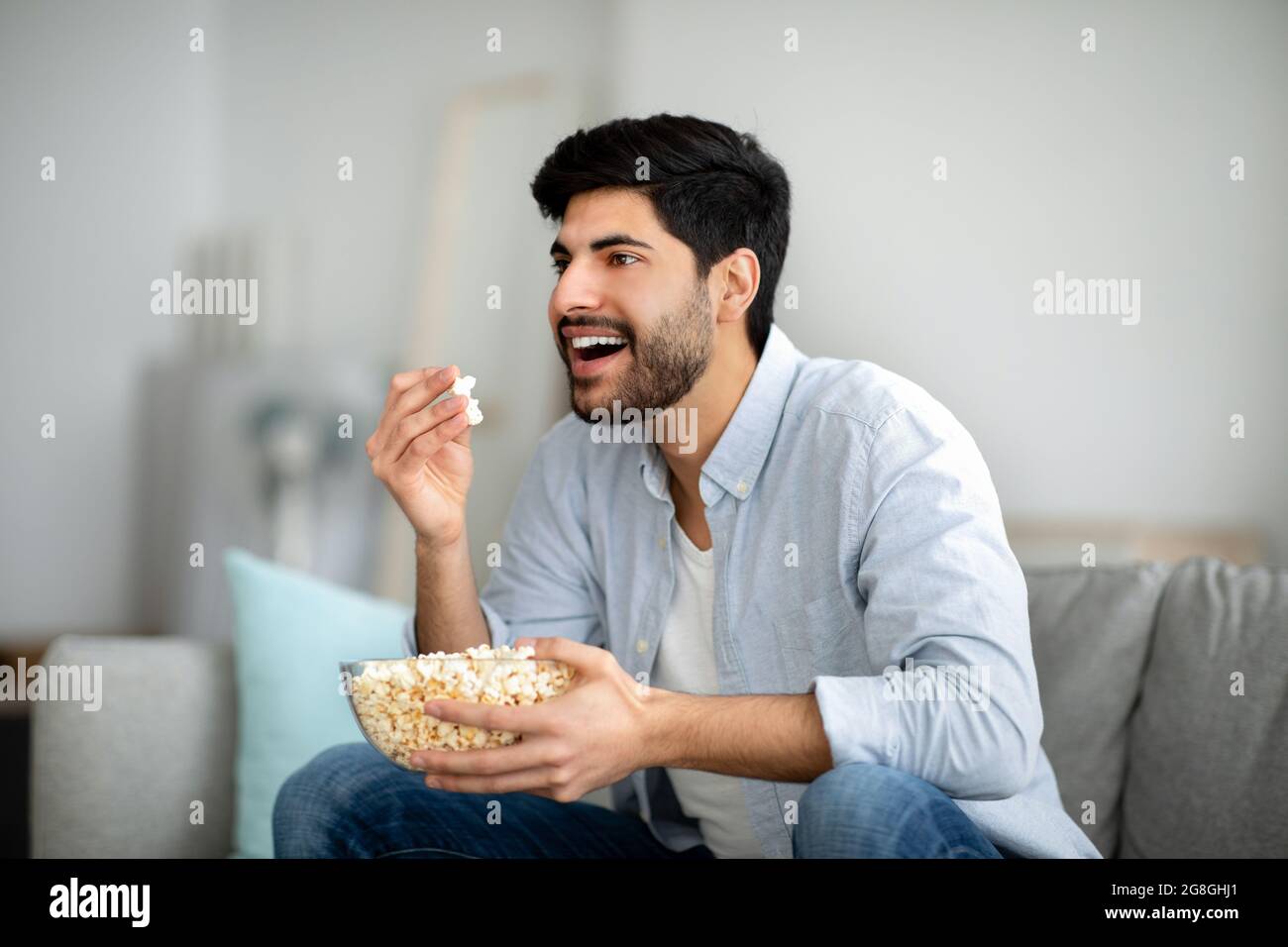 Home Entertainment. Aufgeregter araber, der Popcorn isst und fernsieht, Freizeit zu Hause verbringt, freien Platz Stockfoto