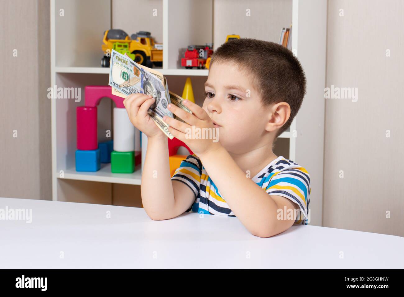 Ein schönes Kind und Dollarscheine. Der Junge denkt darüber nach, wo er das Geld ausgeben soll. Finanzielle Bildung für Kinder Stockfoto