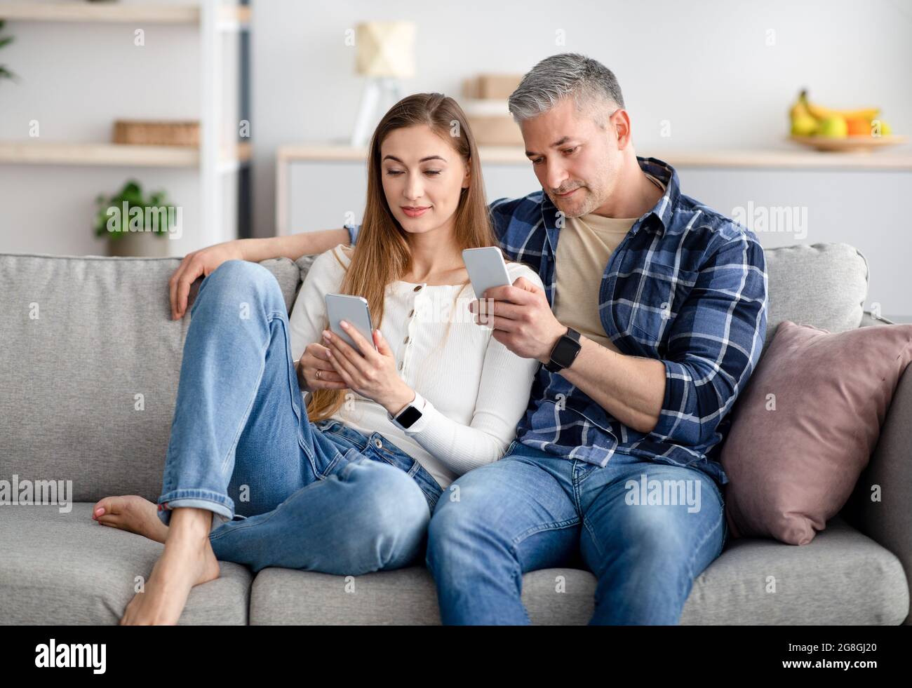 Reifes Paar mit Smartphones, die auf dem Sofa sitzen, sich gegenseitig ignorieren, Online-Spiele spielen, in sozialen Medien surfen Stockfoto