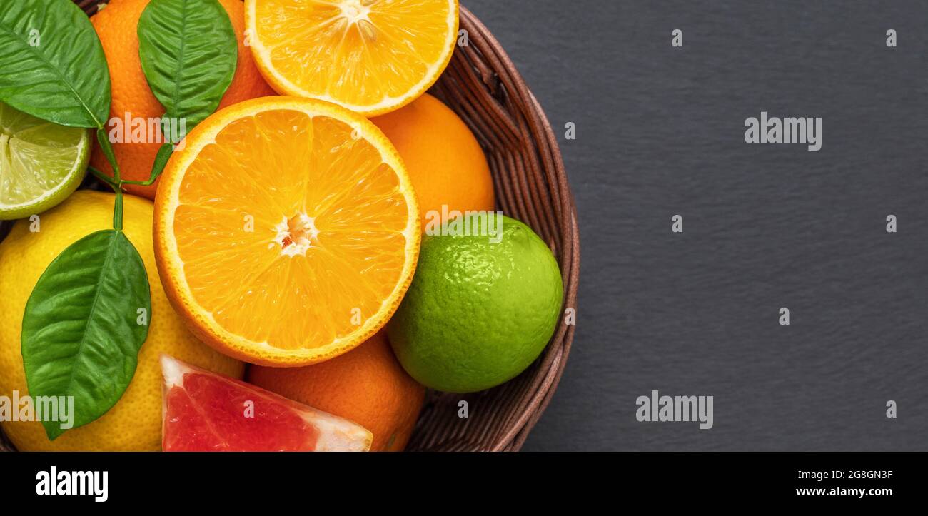 Zitrusfrüchte in einem Korb auf einem grauen Steinhintergrund Nahaufnahme. Mischung aus Zitrusfrüchten. Orange, Zitrone und Limette mit Blättern. Banner. Kopierbereich, Draufsicht, flach Stockfoto