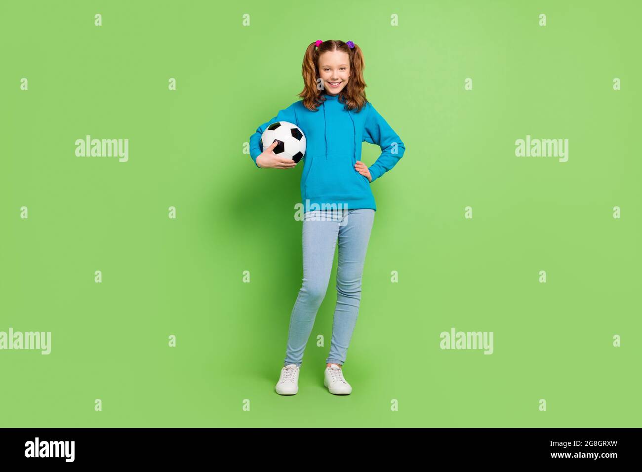 In voller Größe Foto von fröhlichen jungen glücklichen Mädchen halten Hände Fußball Lächeln aktiv isoliert auf grünem Hintergrund Stockfoto