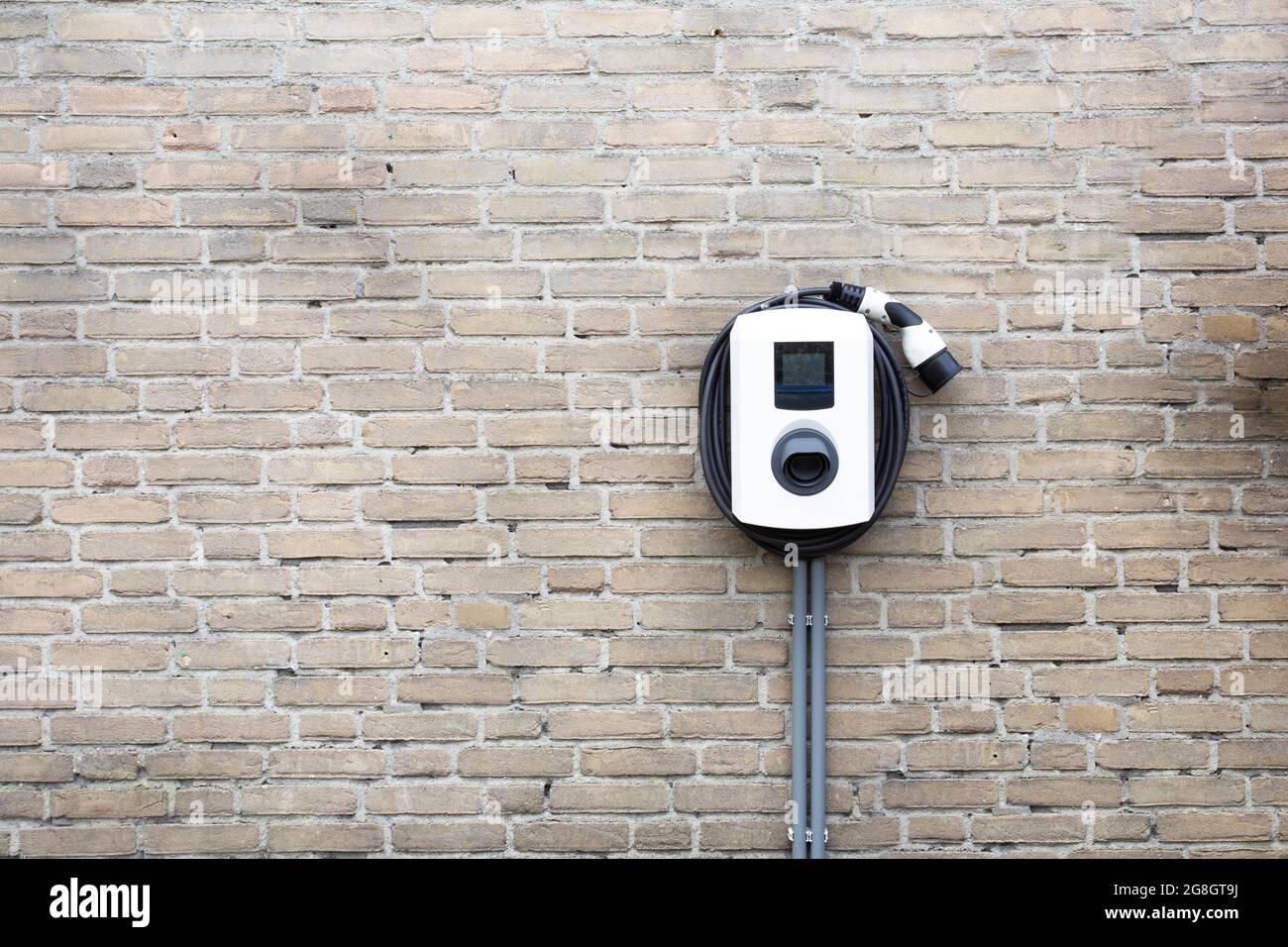Neue Ladestation für Elektroauto an Backsteinwand zu Hause, Ladesäule mit Kopierraum, Stockfoto