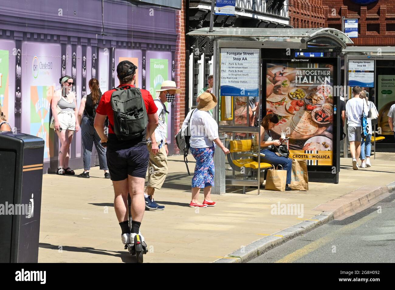 Chester, England - 2021. Juli: Person auf einem E-Scooter, die auf einem Bürgersteig unter Fußgängern im Stadtzentrum unterwegs ist Stockfoto