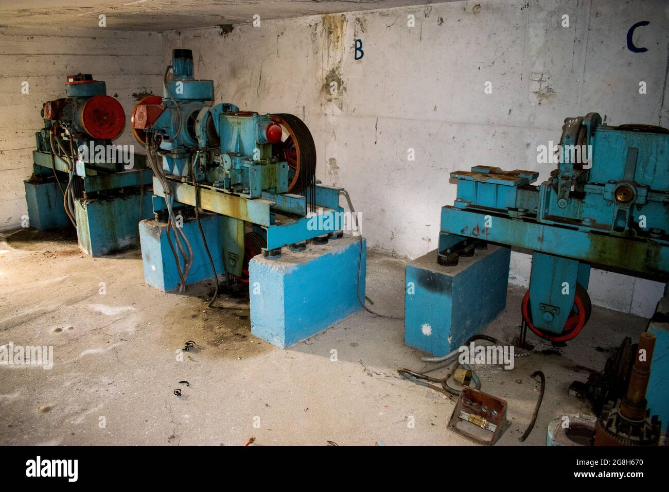 Drei alte Fahrstuhlmotoren in einem Betonlifterraum Stockfoto