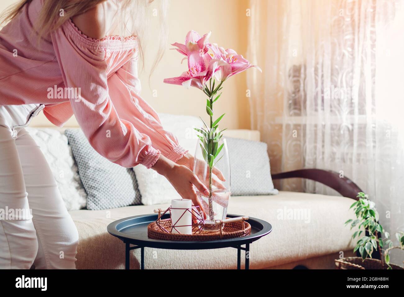 Frau stellt Vase mit rosa Lilienblumen auf den Tisch. Hausfrau kümmert sich um Gemütlichkeit zu Hause. Einrichtung und Einrichtung im Sommer Stockfoto