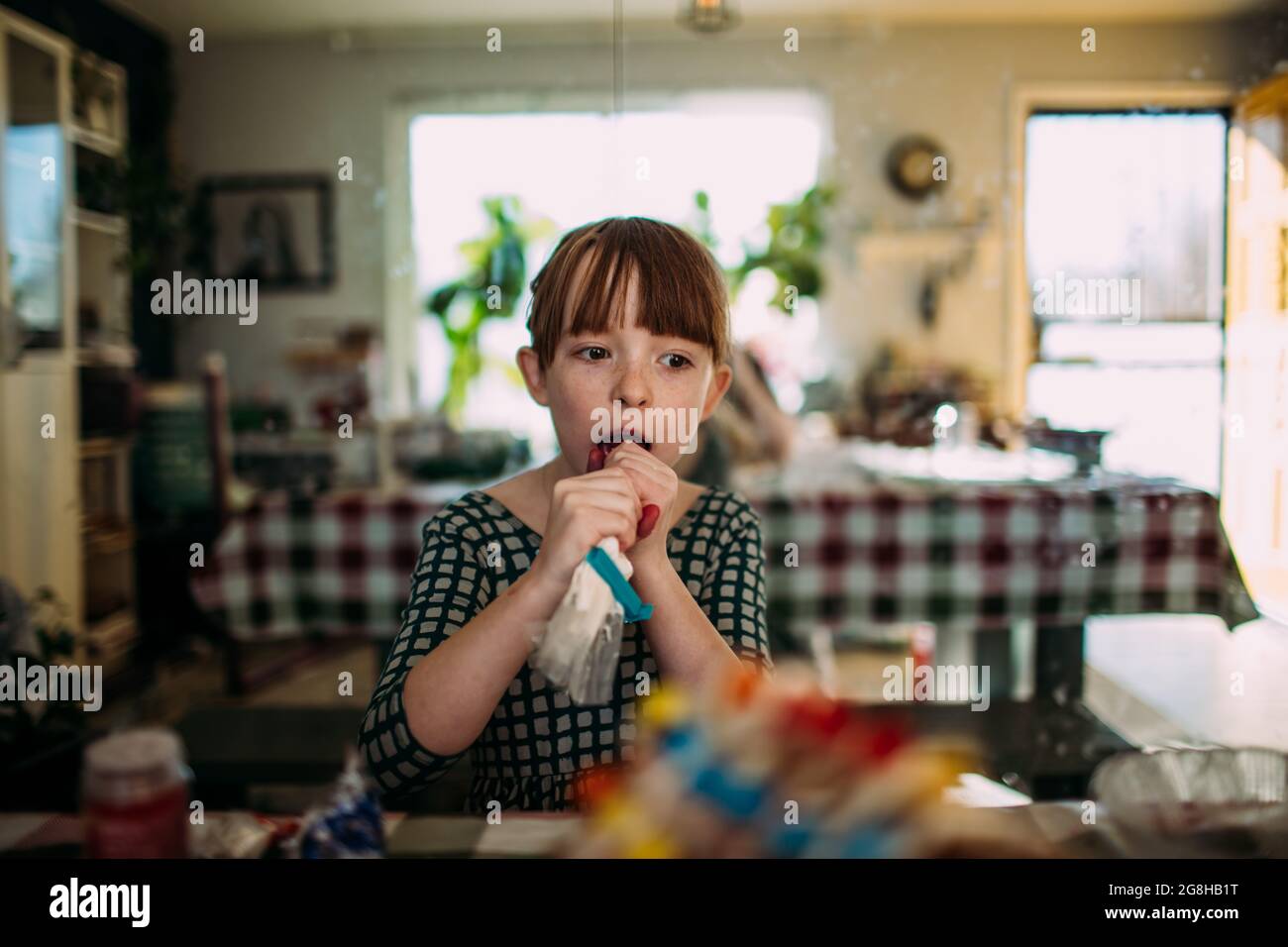 Junges Mädchen lecken Glasur aus der Tasche während der Dekoration Cookies Stockfoto