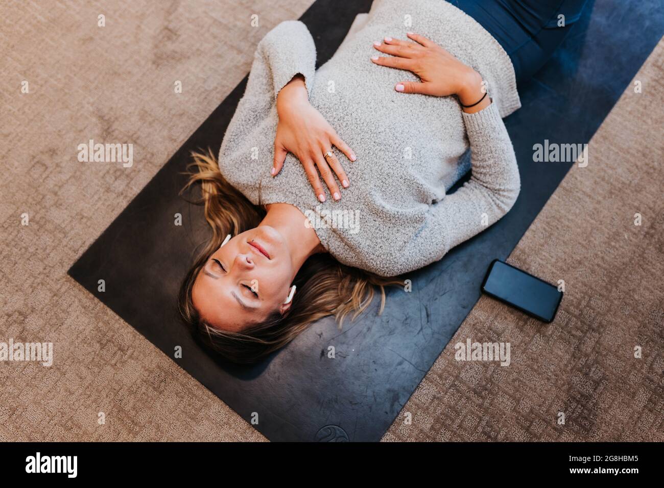 Frau meditiert, während sie in ihrem Haus auf einer Yogamatte liegt Stockfoto