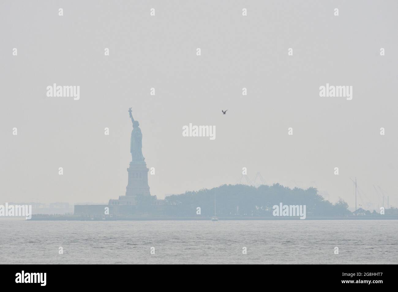 New York, USA. Juli 2021. Die Freiheitsstatue, die vom Battery Park in Manhattan aus gesehen wird, ist in einem dichten Dunst verhüllt, der durch Rauch entsteht, der von den Waldbränden an der Westküste, New York, NY, am 20. Juli 2021, stammt. Im Bundesstaat Oregon und Kalifornien brennen weiterhin massive Blasen. (Foto von Anthony Behar/Sipa USA) Quelle: SIPA USA/Alamy Live News Stockfoto