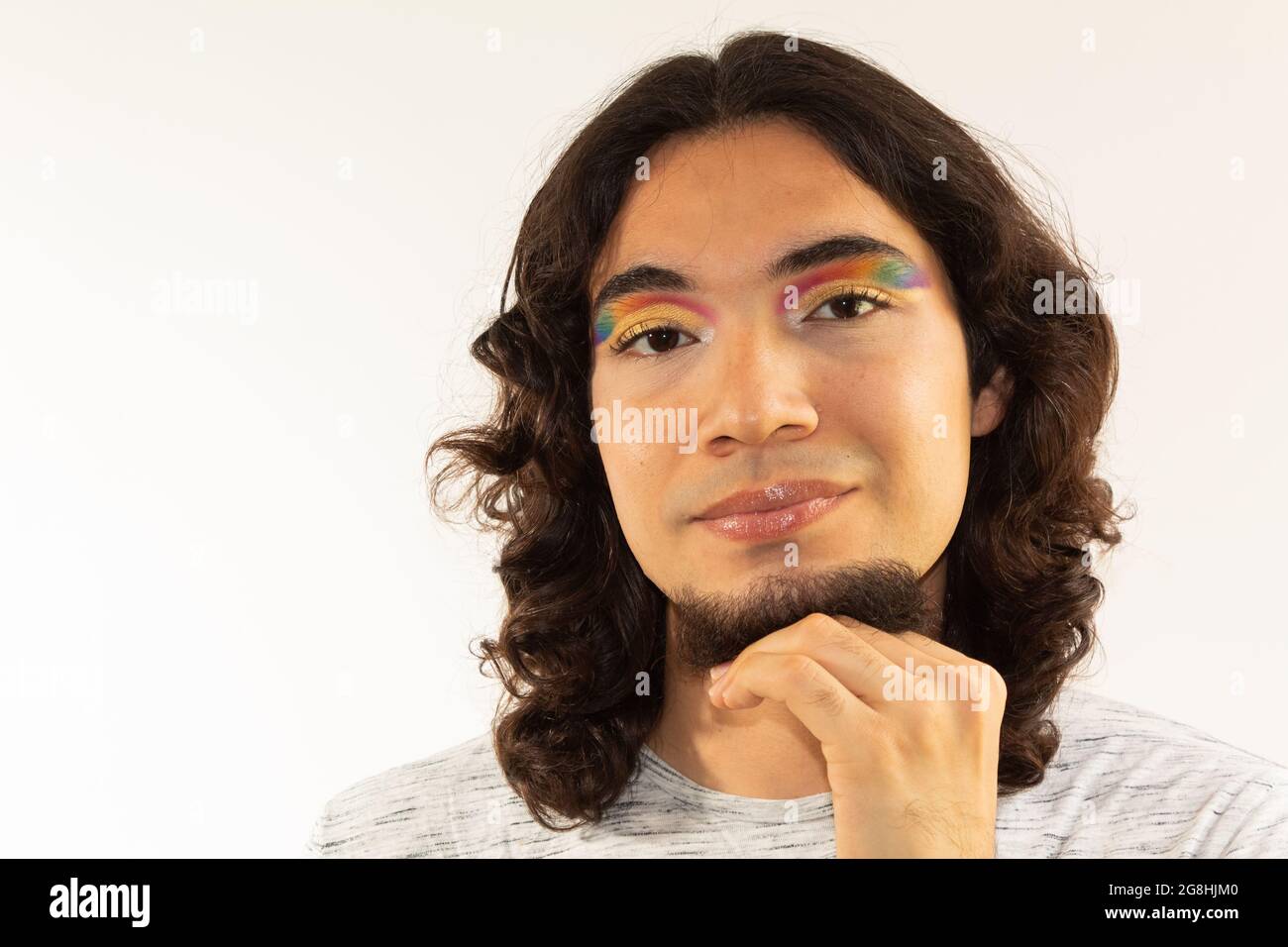 Porträt eines schwulen Mannes in Make-up mit einem Regenbogen in den Augen auf einem weißen Hintergrund lächelnd Stockfoto