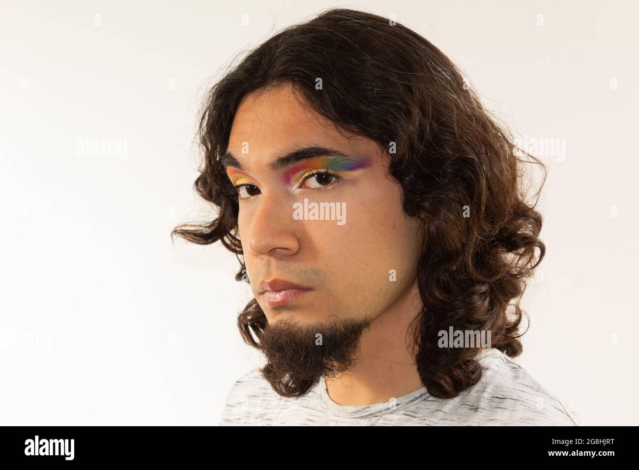 Porträt eines schwulen Mannes, der mit einem Regenbogen in den Augen auf einem weißen Hintergrund mit einem ernsten Gesicht gemacht wurde Stockfoto