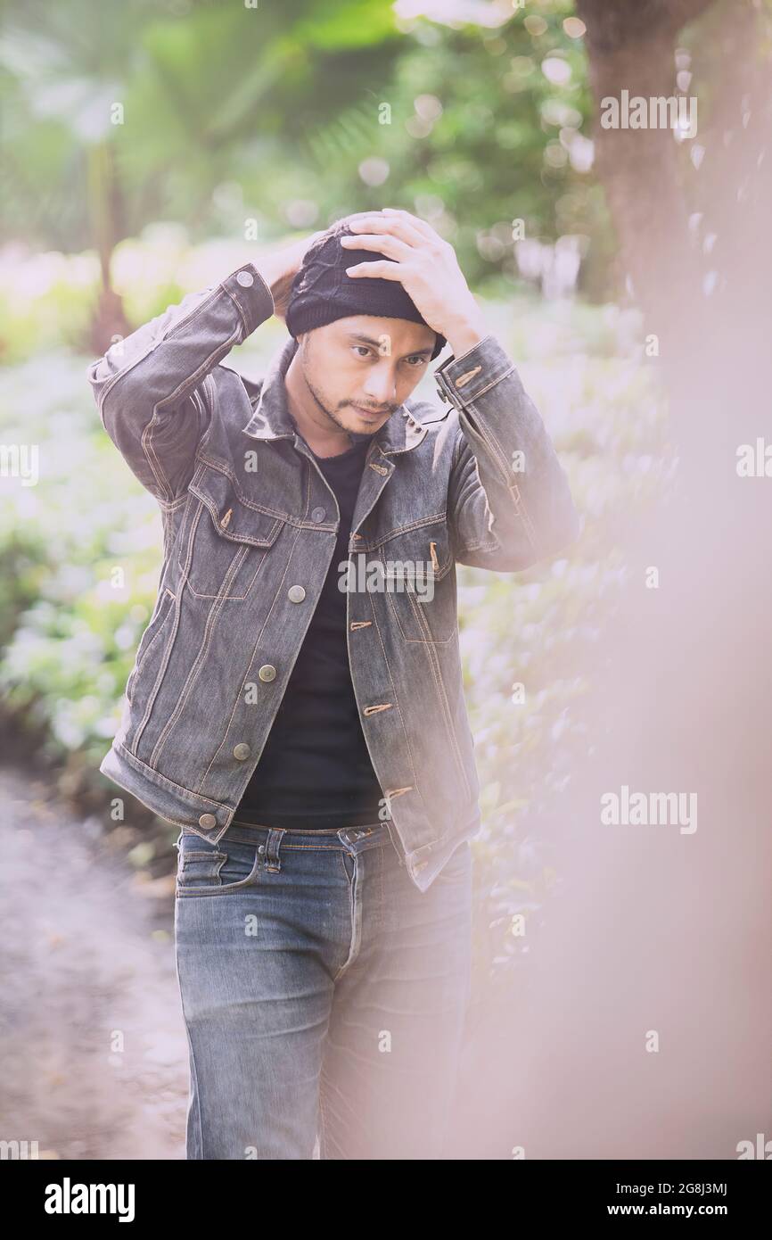 Attraktiver Mann in Jeans trägt eine hat.in mitten in Natur, Bäumen und Sonnenlicht Stockfoto