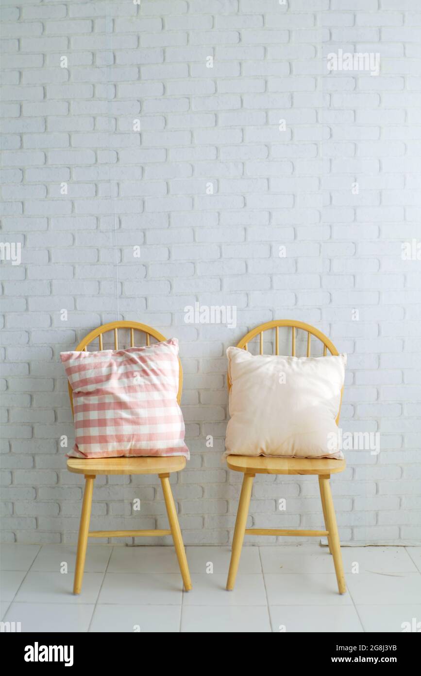 2 Holzstühle auf weißem Backstein-Hintergrund.Es stehen 2 niedliche Kissen zur Verfügung.leerer Platz für Text Stockfoto