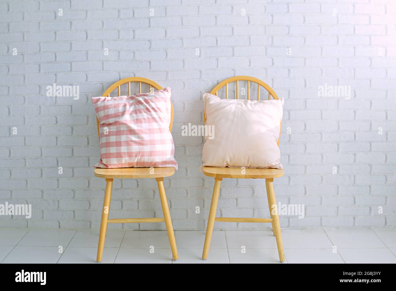 2 Holzstühle auf weißem Backstein-Hintergrund.Es stehen 2 niedliche Kissen zur Verfügung.leerer Platz für Text Stockfoto