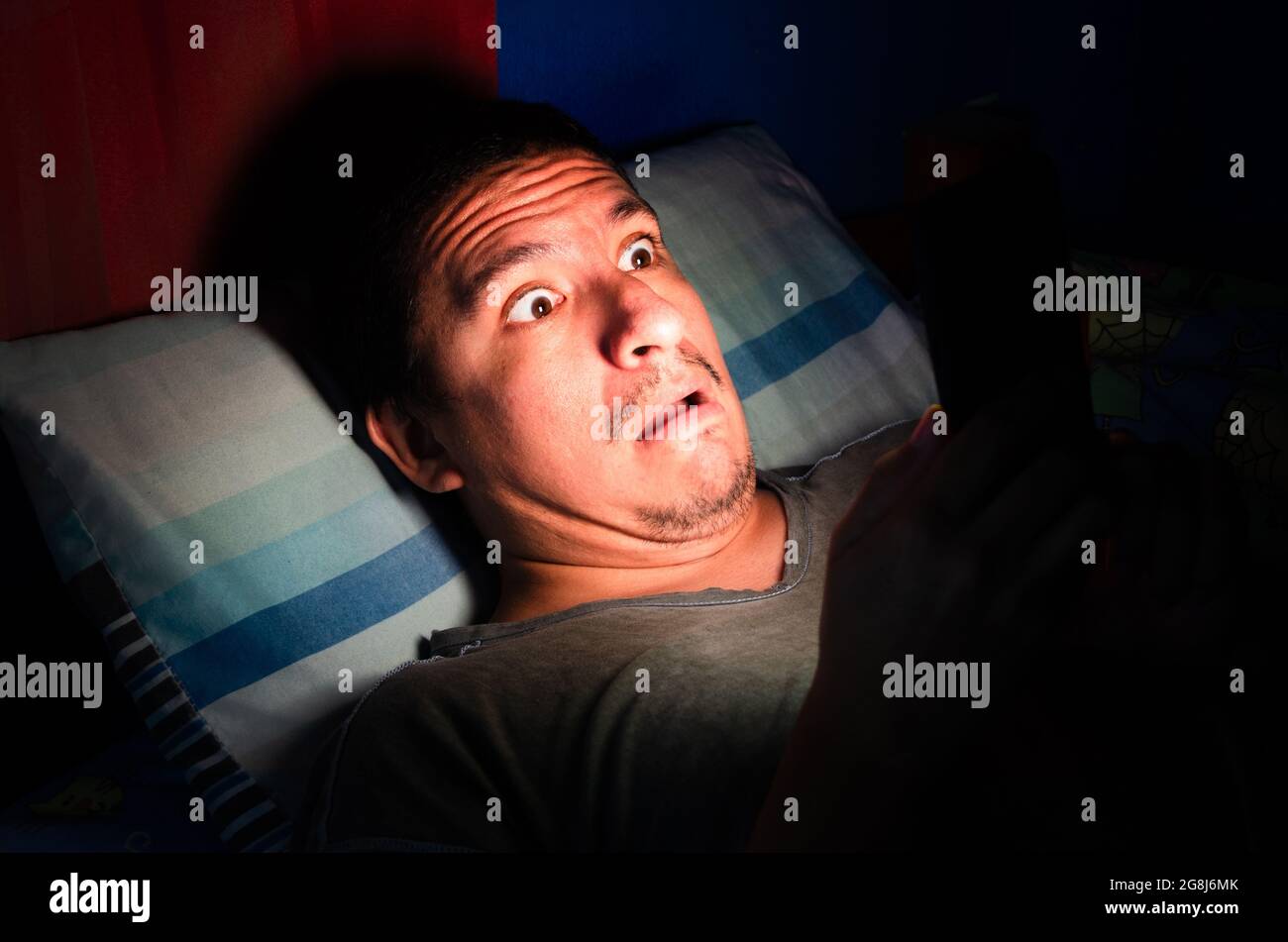 Ein ängstlicher und wach aufwachender Mann schaut nachts im Dunkeln auf sein Telefon. Stockfoto
