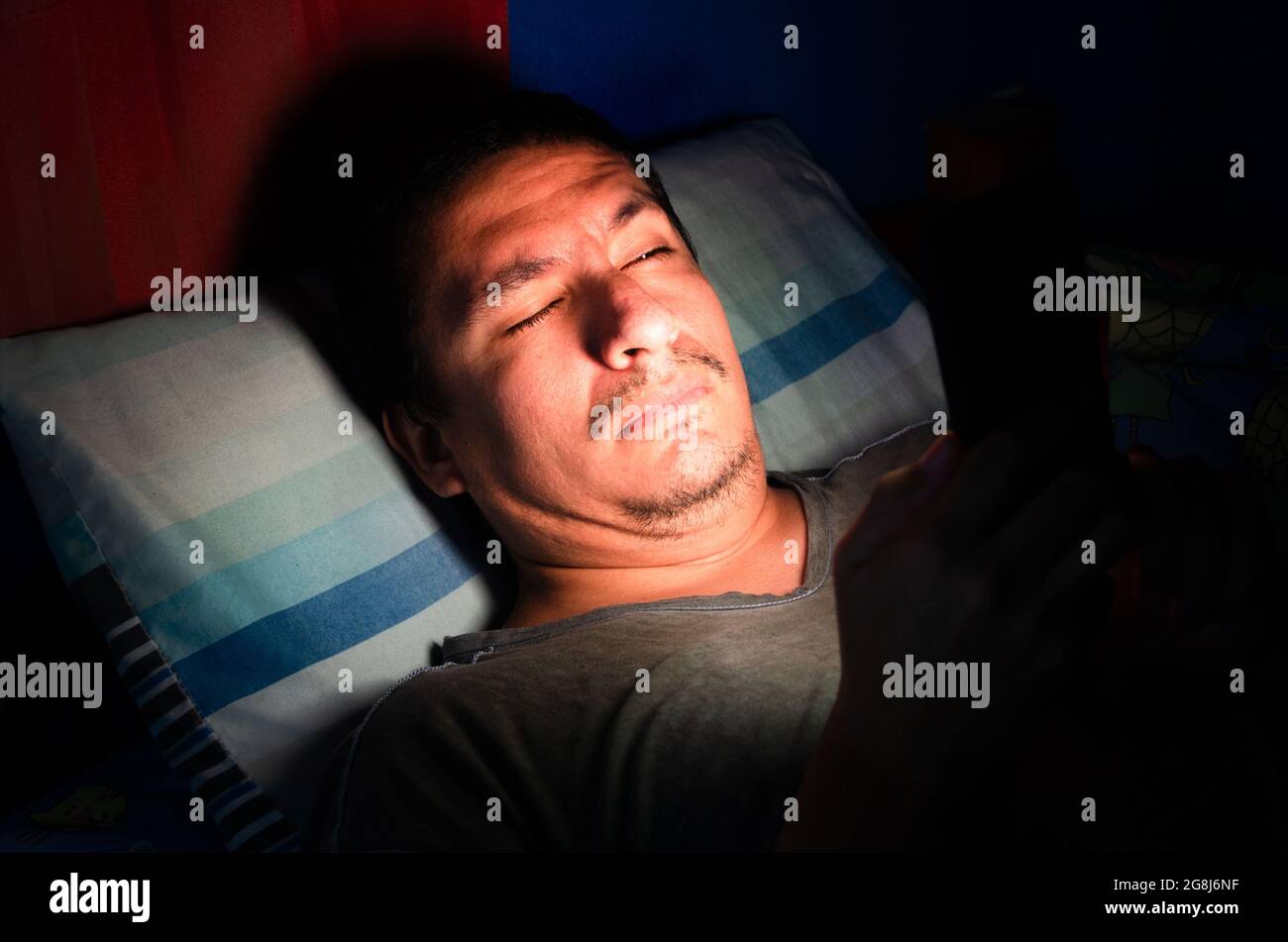 Mann, der sein Mobiltelefon im Bett benutzte Stockfoto