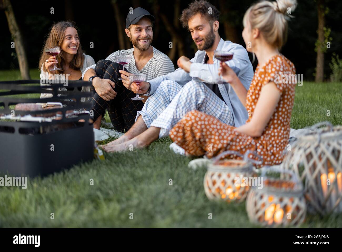 Freunde sitzen zusammen beim Picknick mit Grill und Wein Stockfoto