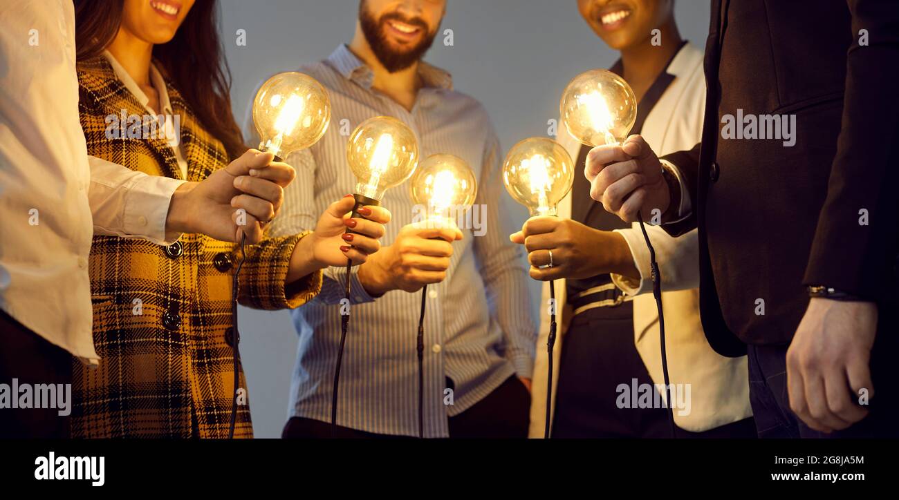 Glückliche Geschäftsleute, die Glühbirnen als Metapher für den Austausch von Ideen in der kreativen Gemeinschaft halten Stockfoto