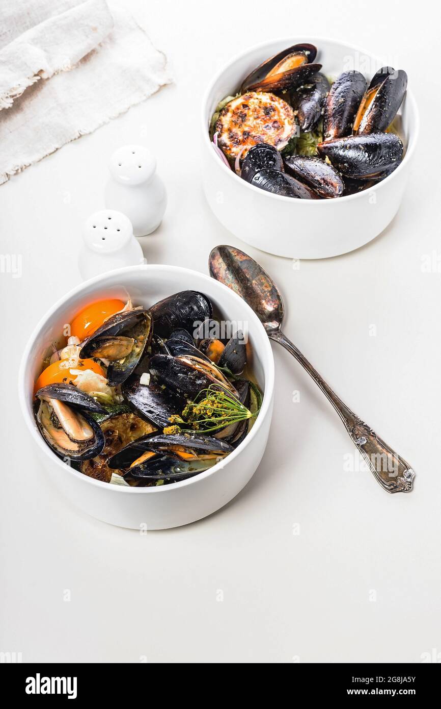 Muscheln mit Gemüse und Kräutern. Zwei Portionen Muscheln in weißen Schalen auf hellem Hintergrund. Gesunde, leckere und leckere Bio-Meeresfrüchte. Traditi Stockfoto