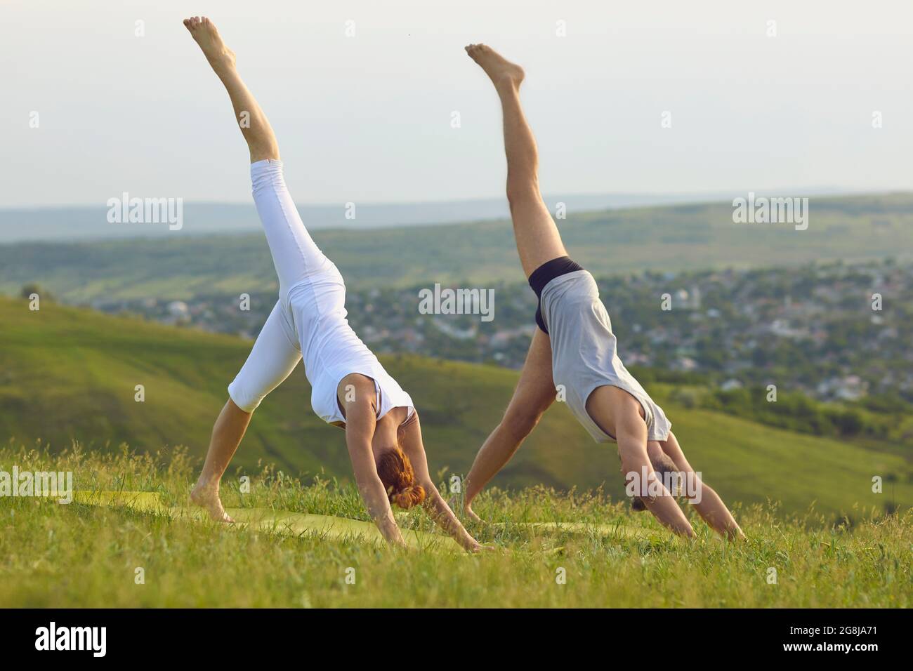 Mann und Frau machen zusammen eine einbeinige Down Dog Asana, während sie Yoga in der Natur praktizieren Stockfoto