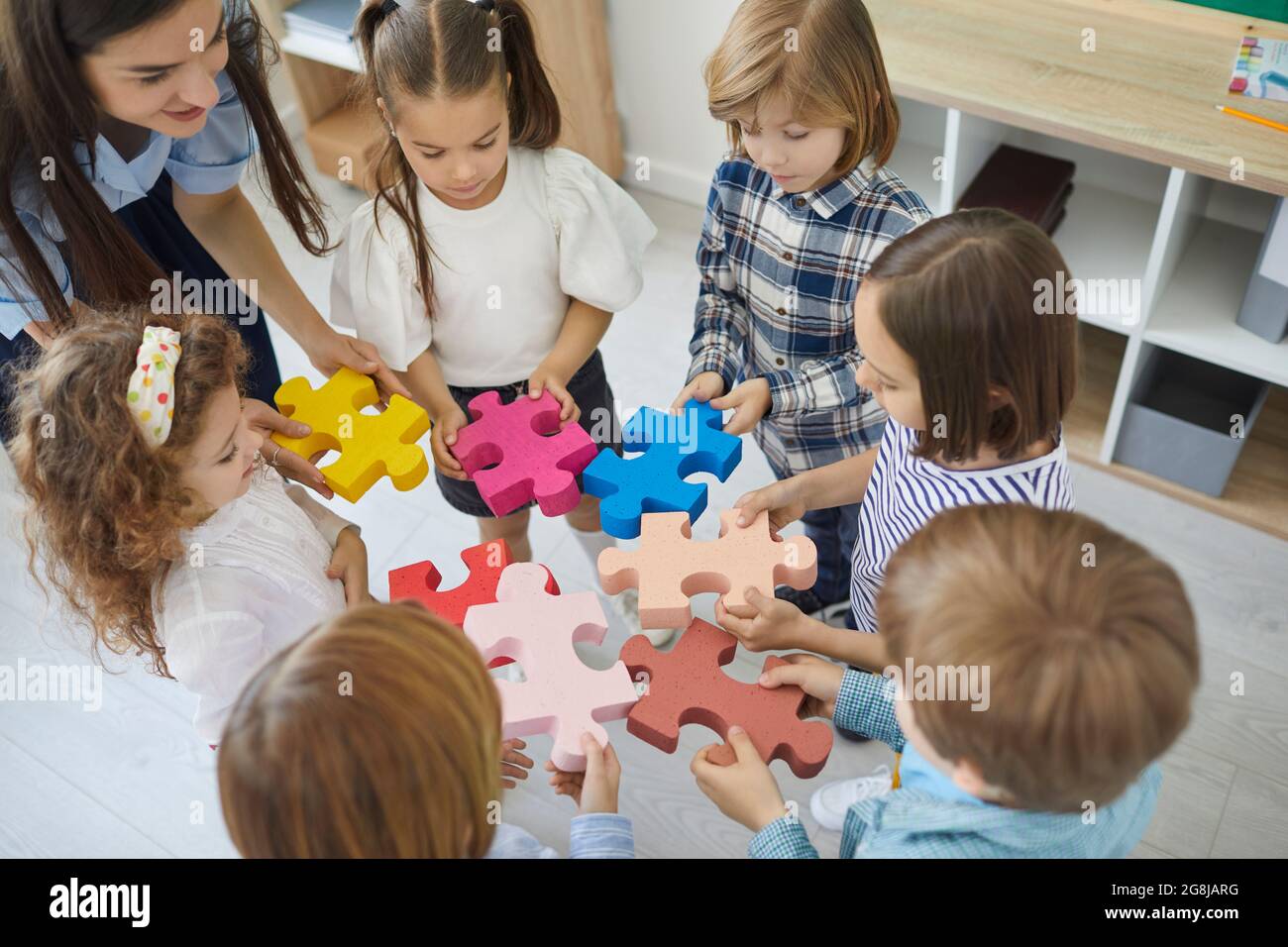 Ein Team von kleinen Kindern verbindet mit ihrem Lehrer Teile eines Puzzles Stockfoto