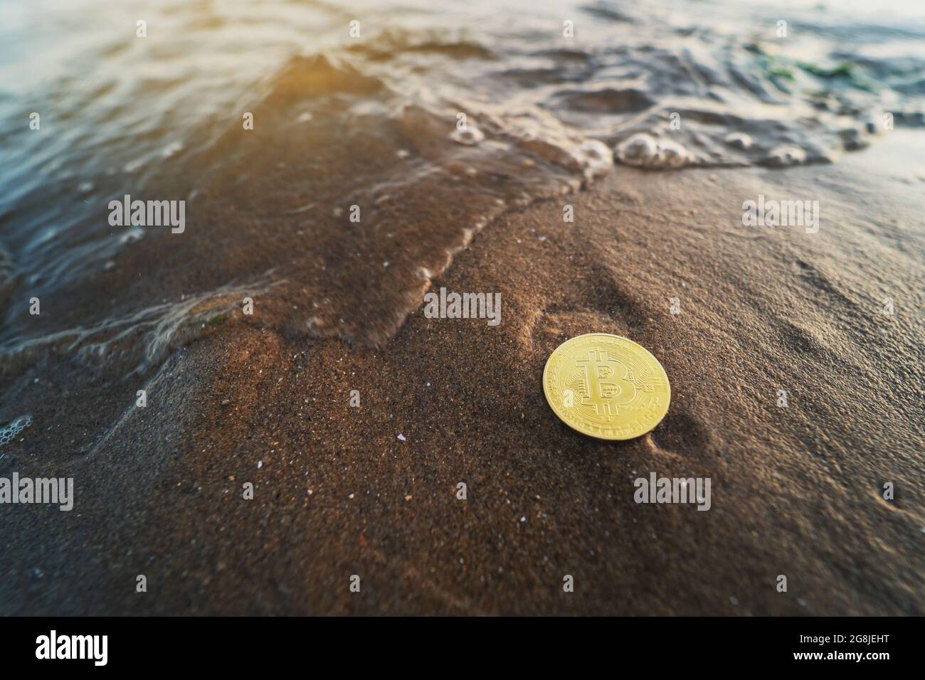 Bitcoin am Strand. Naturhintergrund mit Kopierbereich. Einzelne Goldmünze auf dem Sand neben dem Wasser. Auswirkungen auf die Umwelt, Nutzung von Wasserkraft Stockfoto