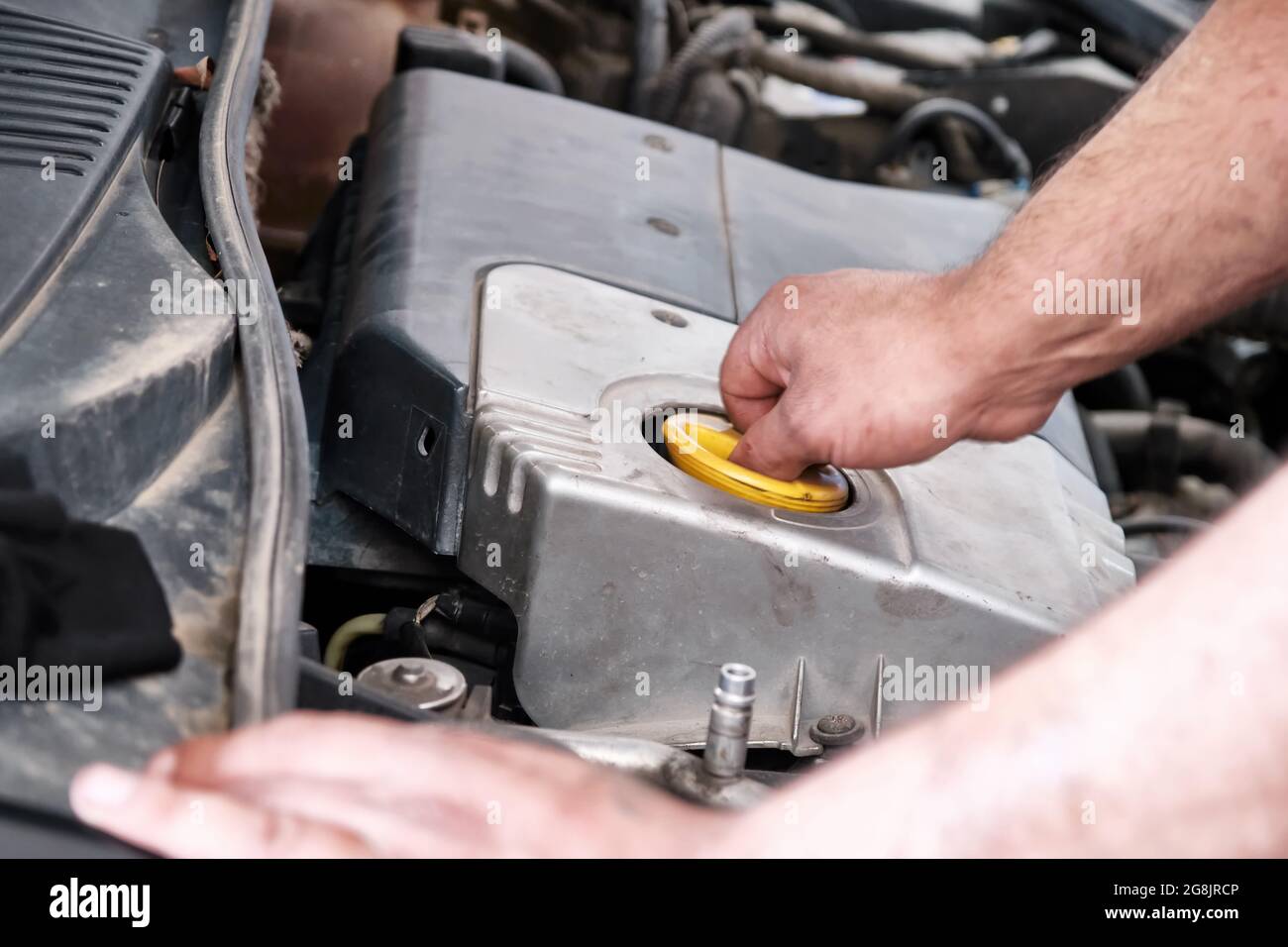 Hände eines Mechanikers, der den Öldeckel des Motormotors öffnet. Fahrzeugöl wechseln oder prüfen. Stockfoto
