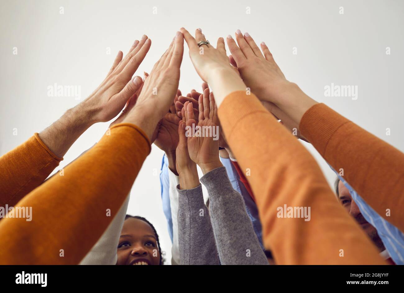 Ein vielseitiges Team glücklicher Geschäftsleute, die ihre Arme heben und sich die Hände verbinden Stockfoto