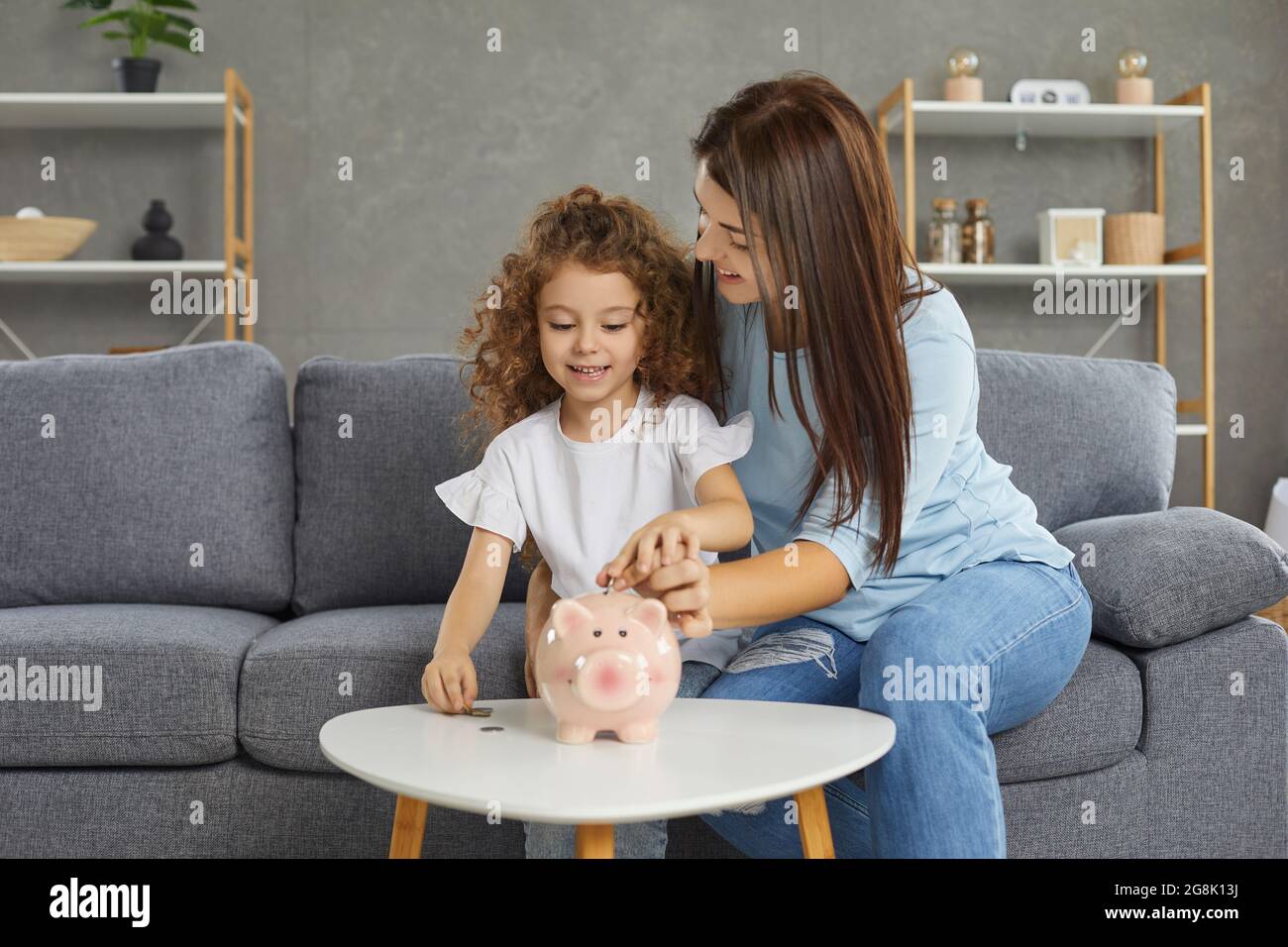 Glückliche Mutter und Kind, die etwas Geld sparen wollen, stecken Münzen in Sparschwein Stockfoto