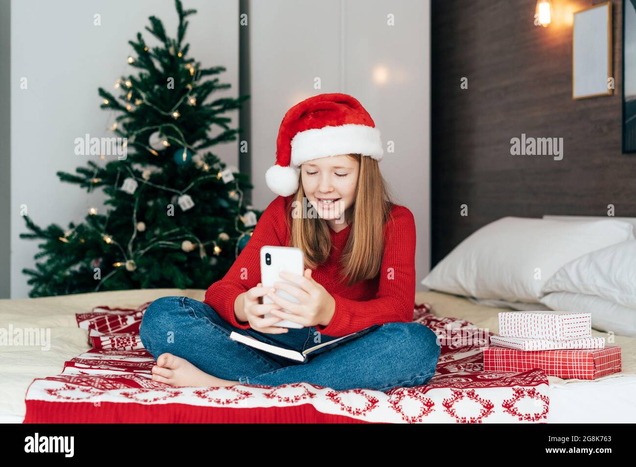 Ein rothaariges Teenager-Mädchen in einem Weihnachtsmann-Hut im Video-Chat auf dem Mobiltelefon. Stockfoto