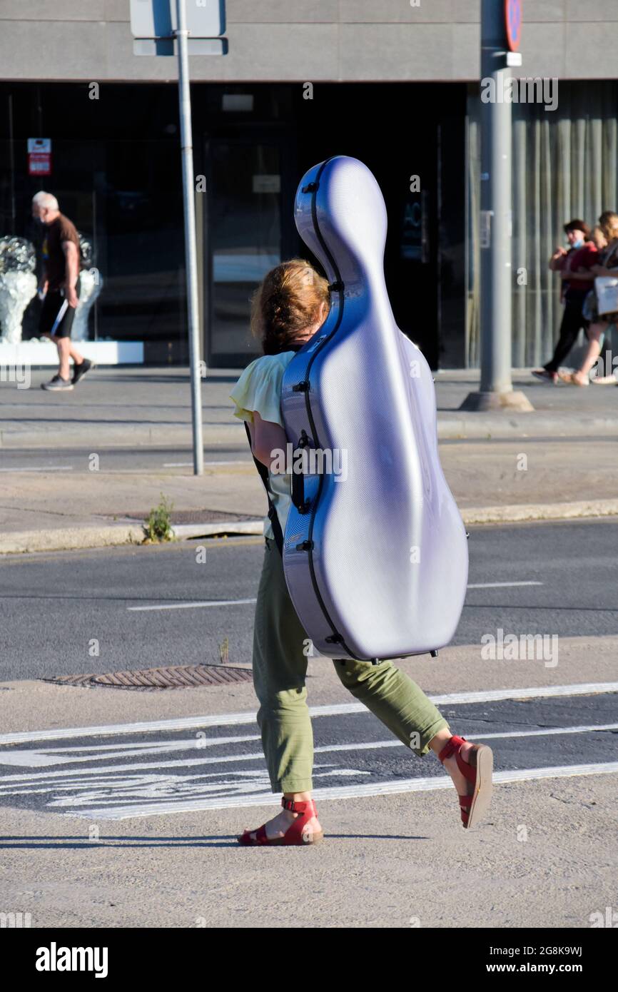 Junge Frau, die in einer Straße mit Cellogehäuse auf ihren Schultern läuft. Stockfoto