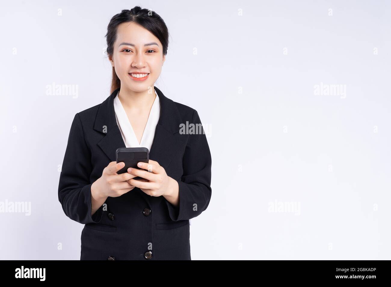 Junge vietnamesische Mitarbeiterin in schwarzem Anzug mit Mobiltelefon und lächelnd Stockfoto