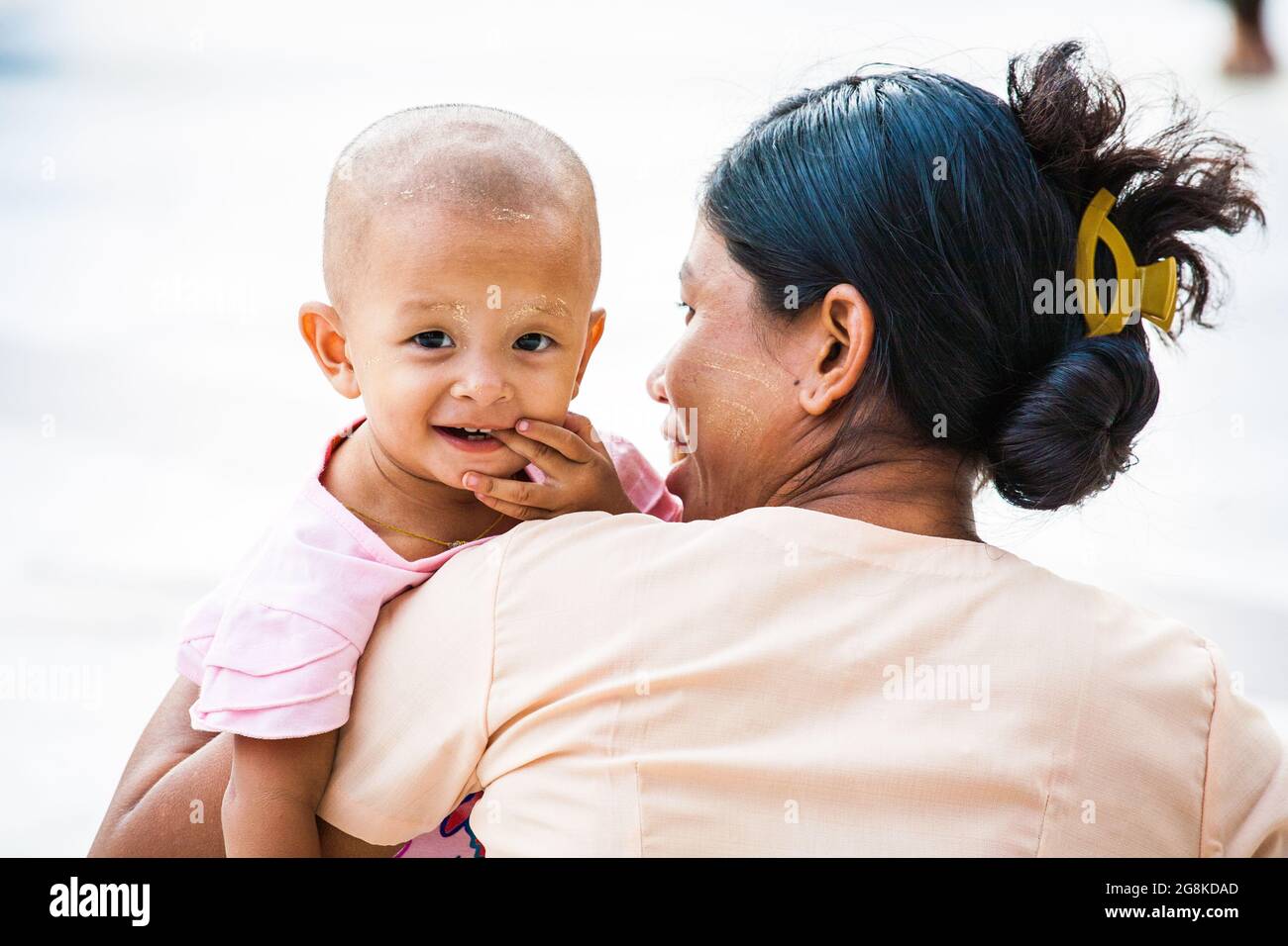 Die burmesische Mutter hält ein kleines Kind mit rasiertem Kopf und lächelt der Kamera, Shwedagon Pagode, Yangon, Myanmar, zu Stockfoto