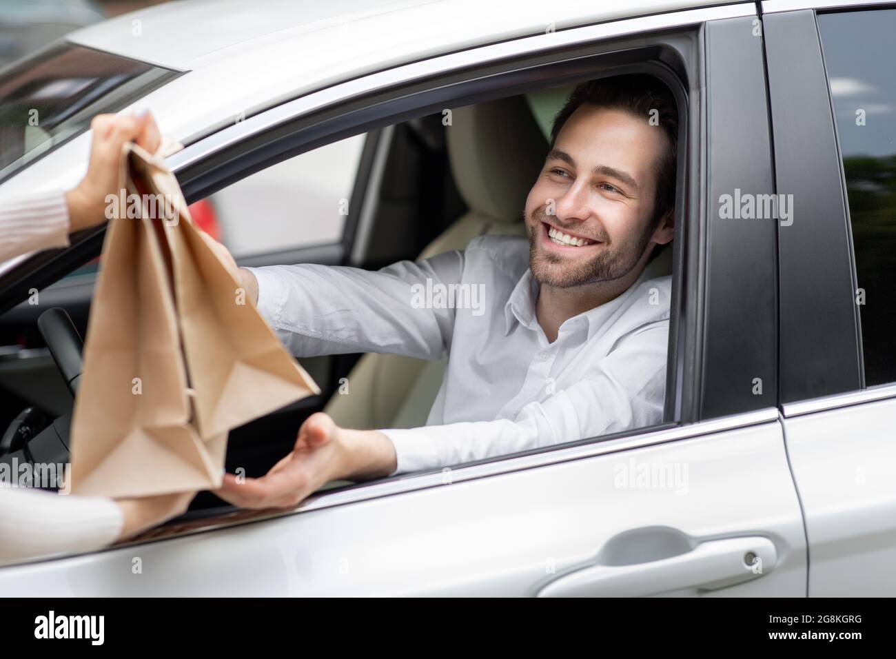 Der Lebensmittellieferungskurier gibt dem Mann im Auto Papiertüten. Lieferung von Sicherheitsnahrung Stockfoto