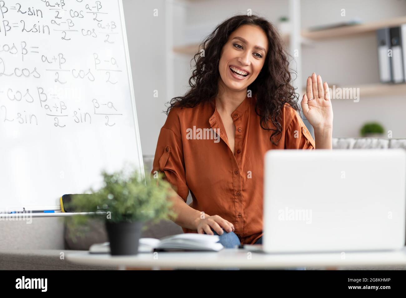 Lächelnde junge Frau, die Online-Studenten Mathematik beibringt und hallo winkt Stockfoto